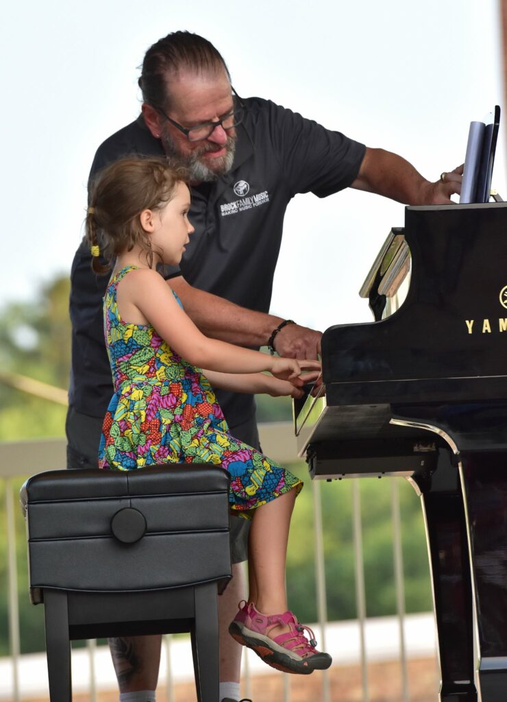 A girl sitting at a piano while an older male teacher points out stuff on sheet music to her.