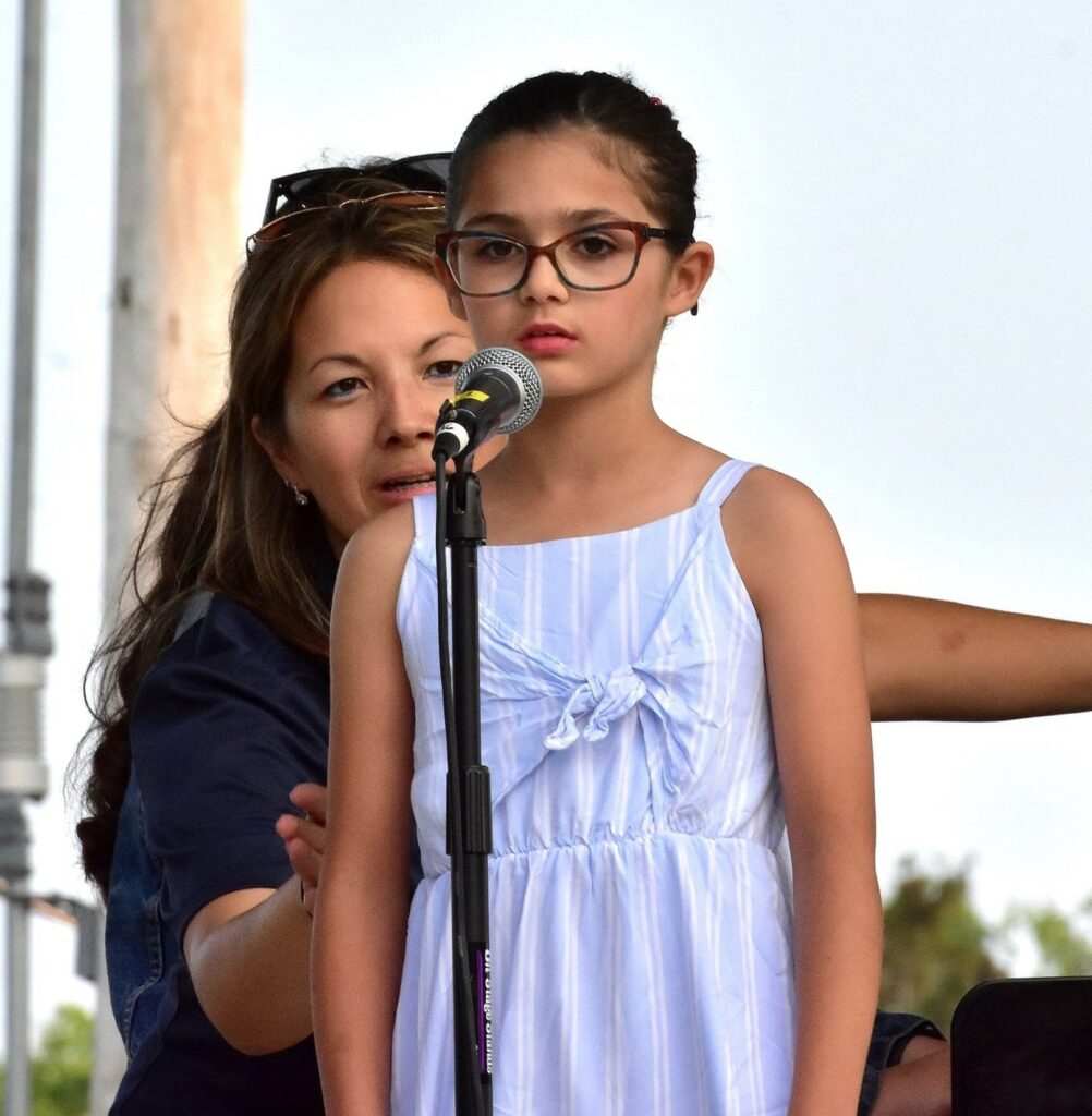 A young girl singing into a microphone with a woman behind her