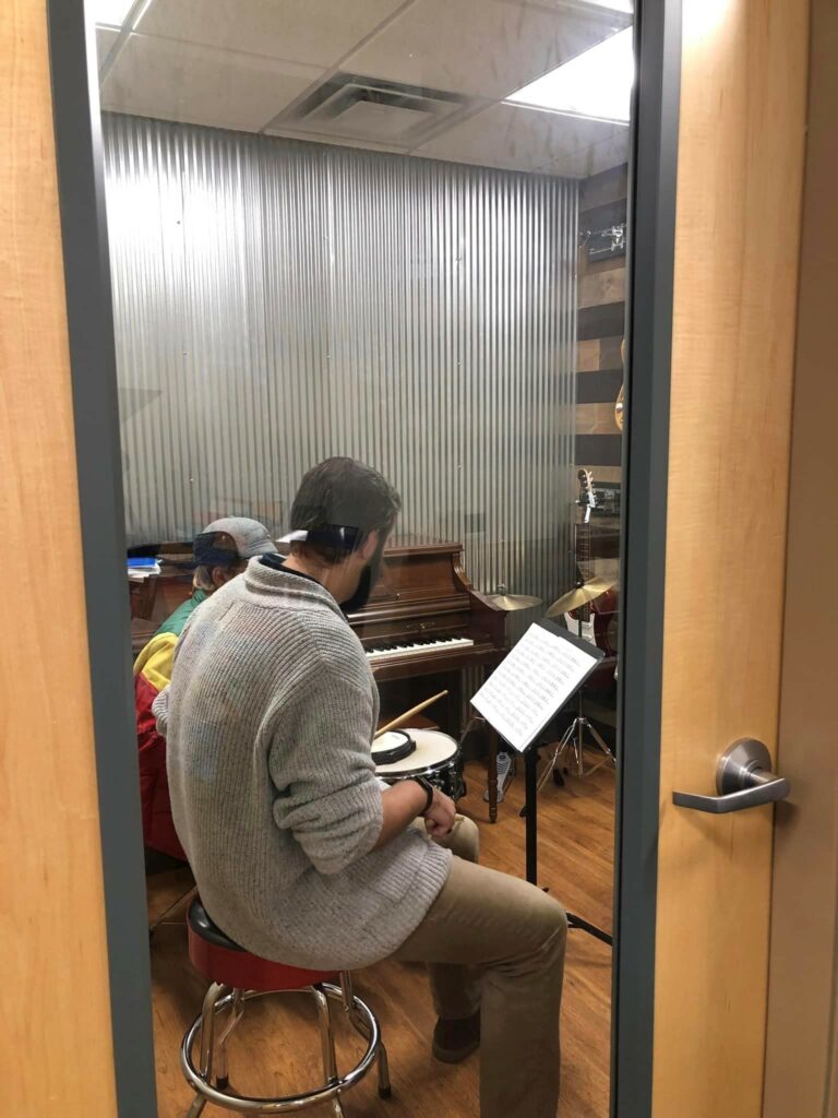 A teacher sitting at a drumset and showing a child how to play